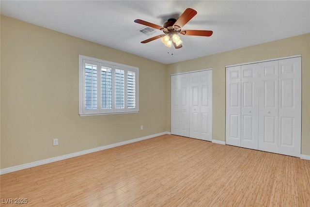 unfurnished bedroom with multiple closets, light wood-type flooring, visible vents, and baseboards