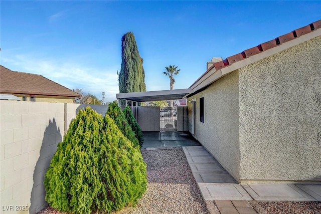 view of side of home with a gate, fence, and stucco siding