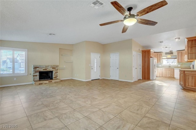 unfurnished living room with light tile patterned floors, a stone fireplace, a sink, visible vents, and a ceiling fan