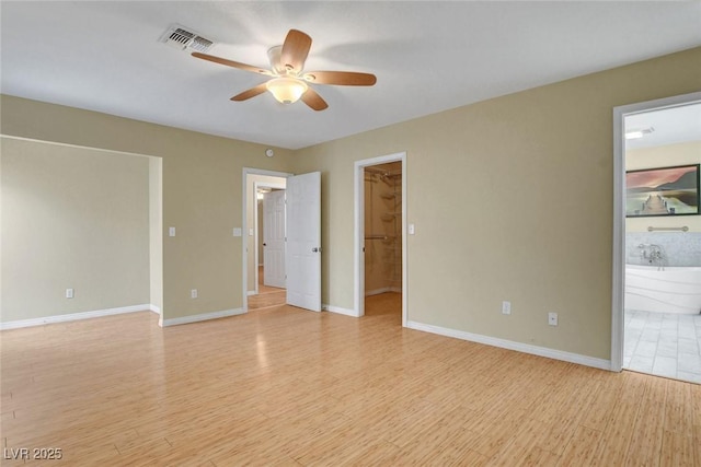 unfurnished bedroom featuring light wood-type flooring, a walk in closet, visible vents, and baseboards