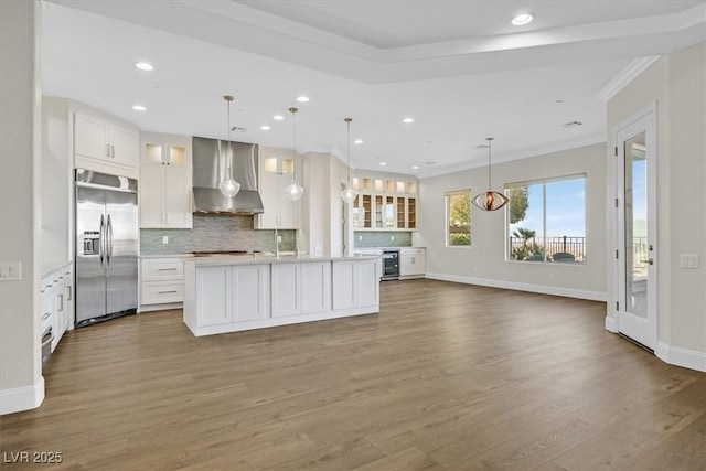 kitchen with built in fridge, light countertops, glass insert cabinets, white cabinets, and wall chimney exhaust hood