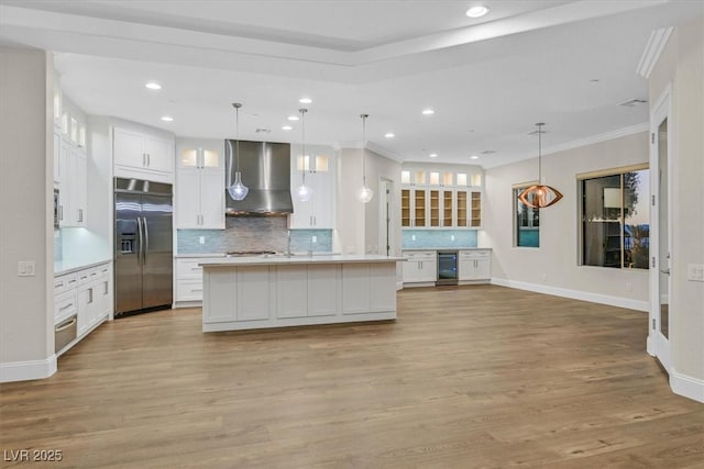 kitchen with beverage cooler, decorative light fixtures, built in refrigerator, light countertops, and wall chimney range hood