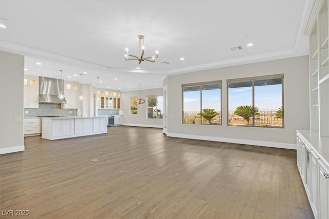 unfurnished living room with wood finished floors, visible vents, baseboards, and an inviting chandelier