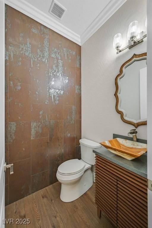 half bathroom featuring toilet, wood finished floors, vanity, visible vents, and crown molding