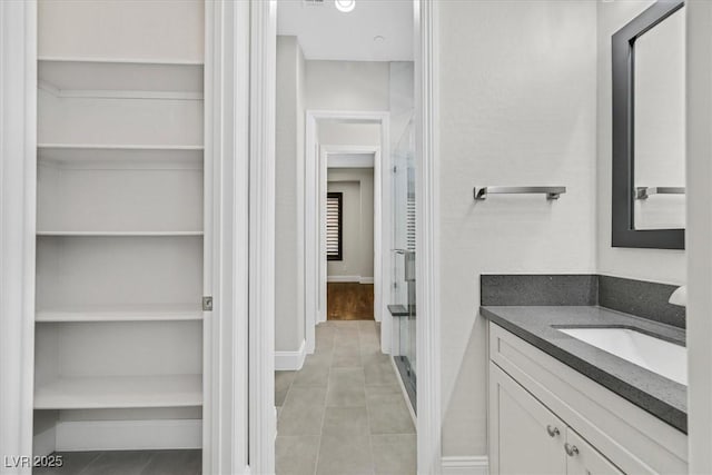 bathroom with baseboards, a walk in closet, vanity, and tile patterned floors