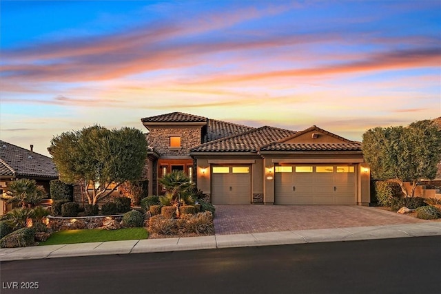 mediterranean / spanish house with driveway, stone siding, a tile roof, an attached garage, and stucco siding