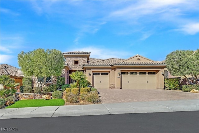 mediterranean / spanish-style house featuring stucco siding, an attached garage, stone siding, driveway, and a tiled roof