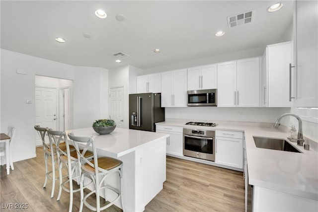 kitchen featuring stainless steel appliances, a sink, visible vents, light countertops, and a center island