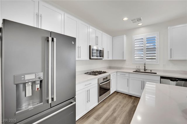 kitchen with visible vents, white cabinets, stainless steel appliances, light countertops, and a sink