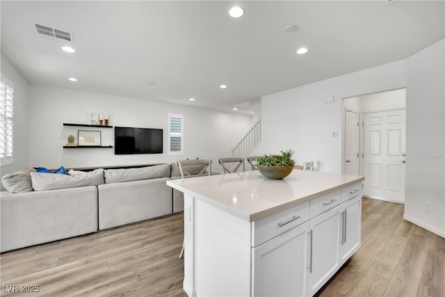 kitchen with visible vents, white cabinetry, open floor plan, light countertops, and a center island