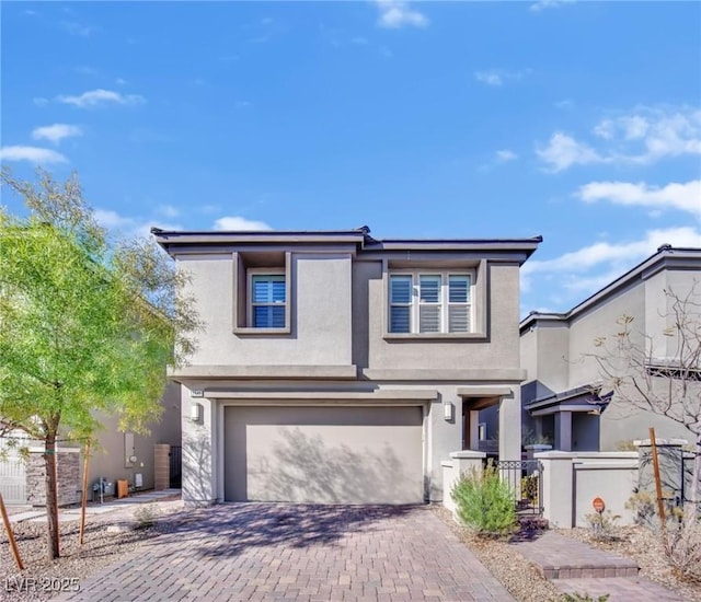 view of front of house with decorative driveway, fence, an attached garage, and stucco siding