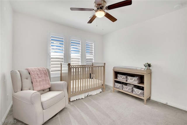 bedroom with a ceiling fan, a nursery area, light colored carpet, and baseboards