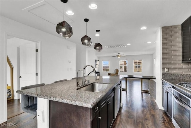 kitchen featuring a breakfast bar, a sink, appliances with stainless steel finishes, light stone countertops, and decorative light fixtures