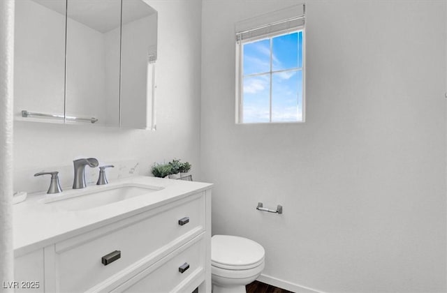 half bath with baseboards, vanity, toilet, and wood finished floors