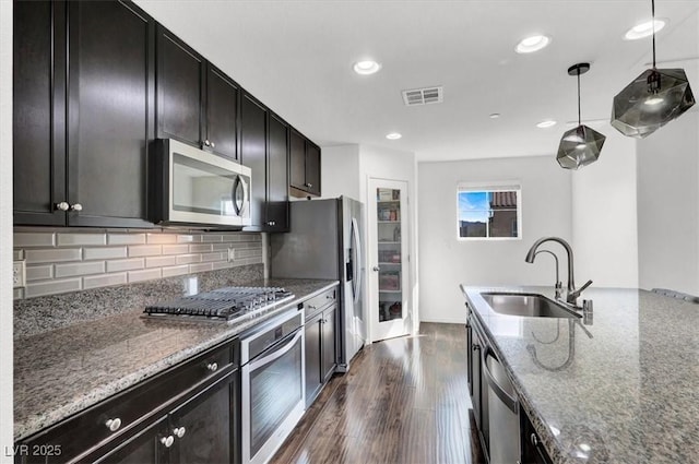 kitchen with stone countertops, dark wood-type flooring, stainless steel appliances, pendant lighting, and a sink