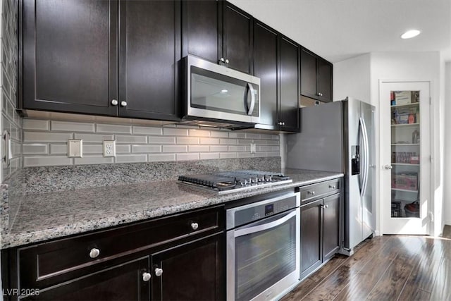 kitchen with light stone counters, appliances with stainless steel finishes, decorative backsplash, and dark wood-style flooring