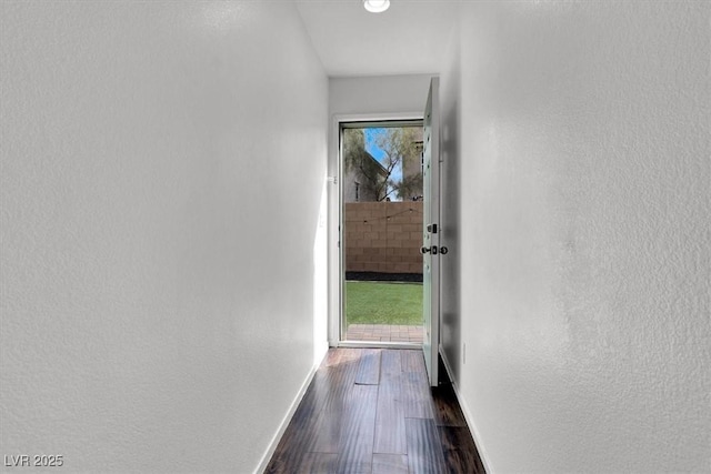 hall featuring a textured wall, dark wood finished floors, and baseboards