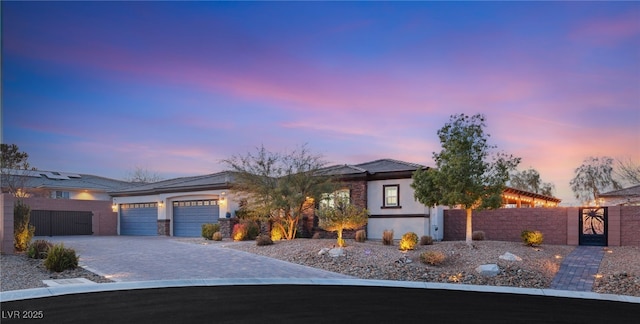 prairie-style home with a gate, fence, stucco siding, a garage, and decorative driveway