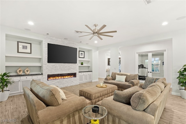 living area featuring light wood finished floors, baseboards, built in features, a stone fireplace, and recessed lighting