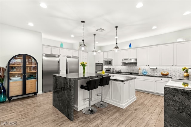 kitchen featuring backsplash, a kitchen island, under cabinet range hood, built in appliances, and a sink