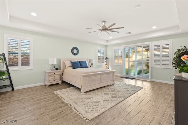 bedroom featuring access to exterior, light wood finished floors, and a tray ceiling