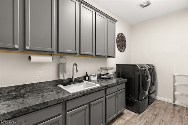 clothes washing area with visible vents, washing machine and clothes dryer, light wood-style flooring, cabinet space, and a sink