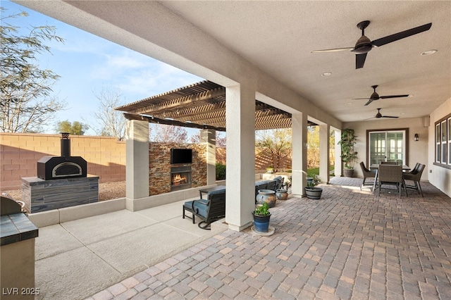 view of patio featuring a ceiling fan, a pergola, fence, a lit fireplace, and outdoor dining area