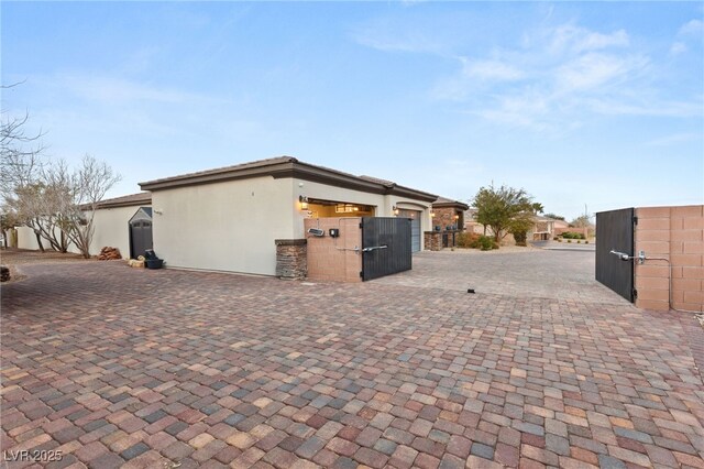 view of home's exterior with stucco siding, an attached garage, decorative driveway, and a gate