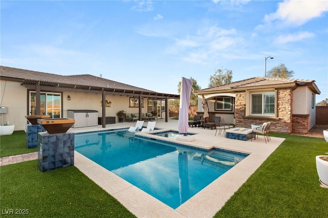 rear view of property with an outdoor fire pit, a yard, stucco siding, stone siding, and a jacuzzi