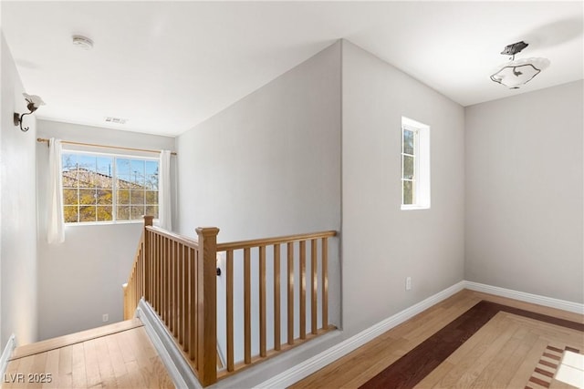 hallway with wood finished floors, visible vents, and baseboards