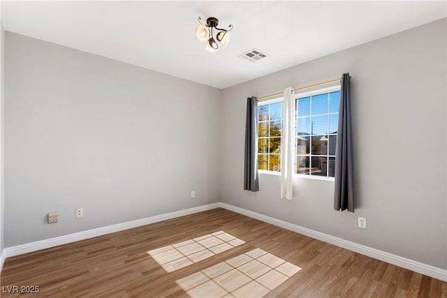 spare room featuring baseboards, visible vents, and wood finished floors