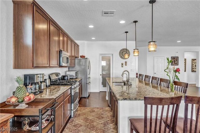 kitchen featuring stainless steel appliances, a sink, visible vents, a kitchen breakfast bar, and an island with sink