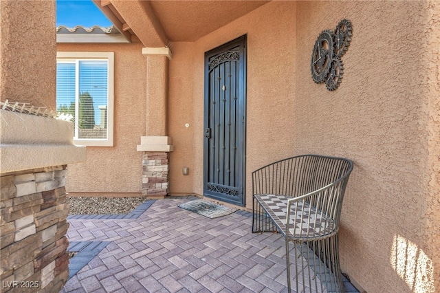 view of exterior entry with a patio, a tiled roof, and stucco siding