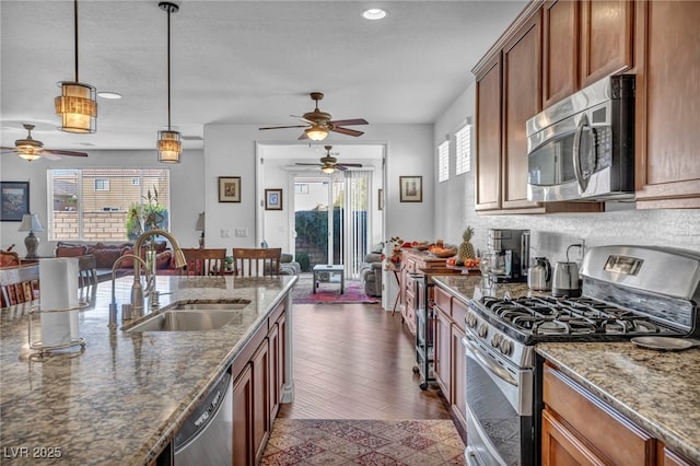 kitchen with brown cabinetry, stainless steel appliances, a sink, and open floor plan