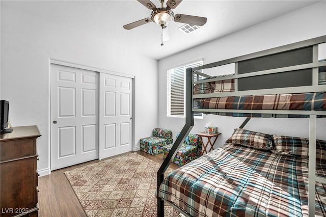 bedroom with baseboards, visible vents, ceiling fan, wood finished floors, and a closet