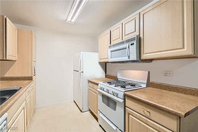 kitchen featuring a textured ceiling, white appliances, light brown cabinets, and baseboards