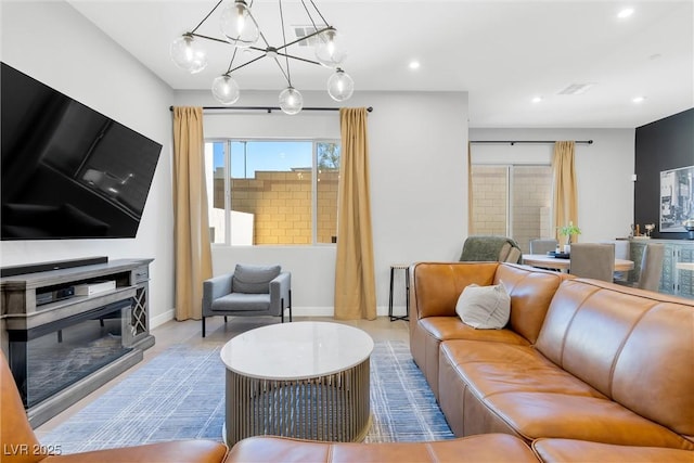 living area featuring a notable chandelier, recessed lighting, visible vents, baseboards, and a glass covered fireplace