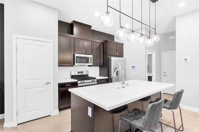 kitchen with a center island with sink, appliances with stainless steel finishes, a kitchen breakfast bar, light countertops, and dark brown cabinets