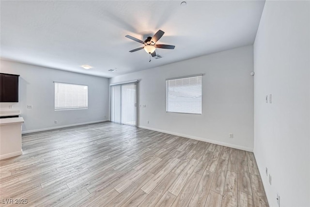 unfurnished living room featuring light wood finished floors, visible vents, baseboards, and a ceiling fan