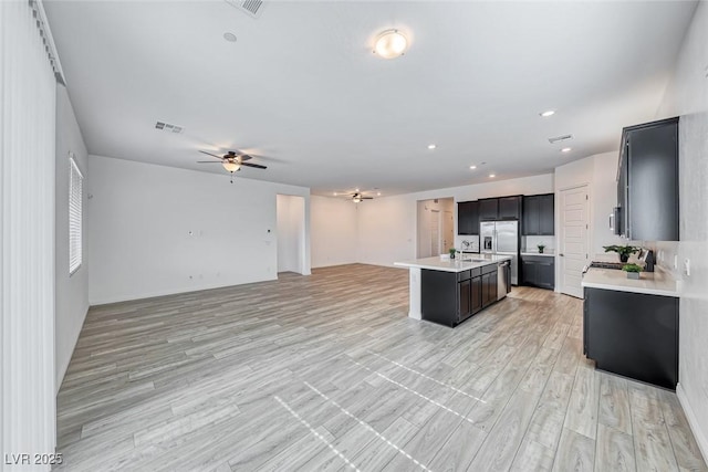 kitchen with a center island with sink, visible vents, a ceiling fan, open floor plan, and light countertops