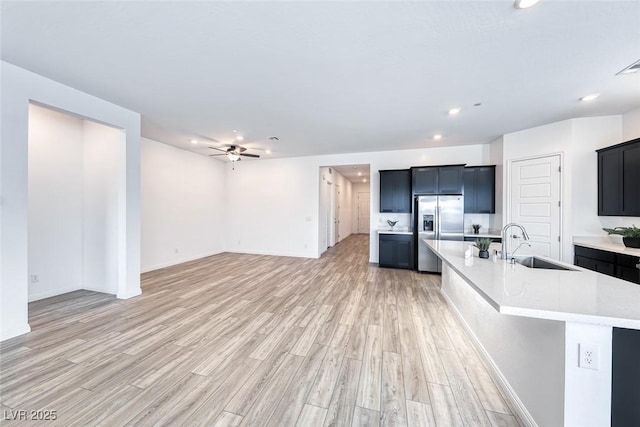 kitchen featuring an island with sink, stainless steel fridge, open floor plan, and dark cabinets