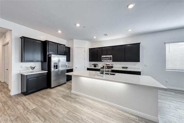 kitchen featuring stainless steel appliances, dark cabinetry, a center island with sink, and visible vents