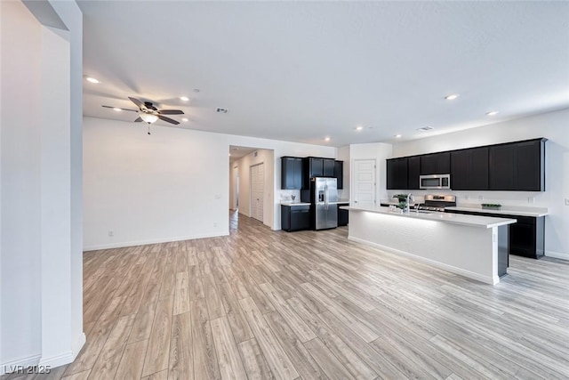 kitchen with open floor plan, light countertops, appliances with stainless steel finishes, dark cabinetry, and an island with sink