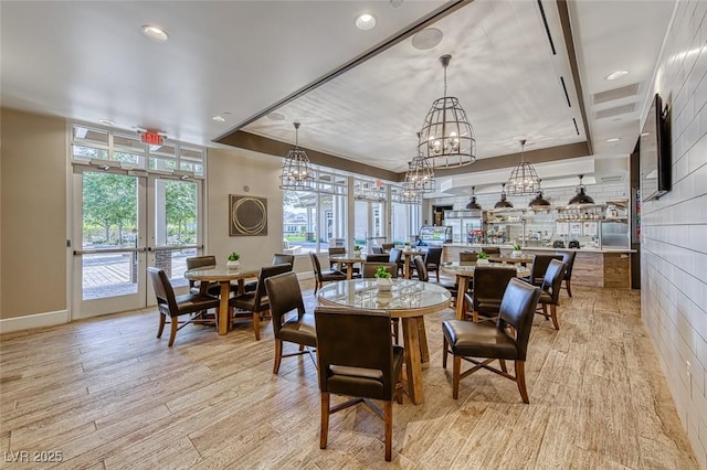 dining area featuring light wood-style floors, recessed lighting, a raised ceiling, and french doors