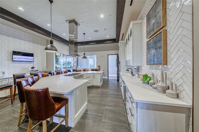 kitchen featuring a breakfast bar area, hanging light fixtures, light countertops, white cabinetry, and backsplash