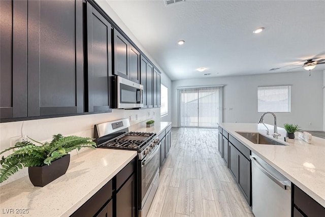 kitchen featuring light stone counters, light wood-style flooring, a sink, visible vents, and appliances with stainless steel finishes