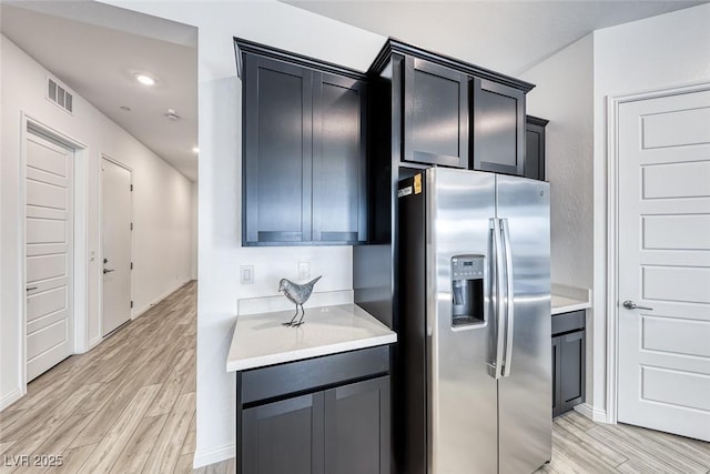 kitchen featuring visible vents, light wood-style floors, light countertops, dark cabinetry, and stainless steel refrigerator with ice dispenser