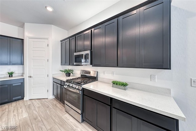 kitchen featuring appliances with stainless steel finishes, light wood-type flooring, dark cabinets, and light stone counters