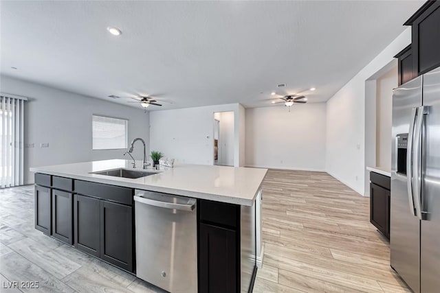 kitchen with a center island with sink, appliances with stainless steel finishes, light countertops, dark cabinetry, and a sink