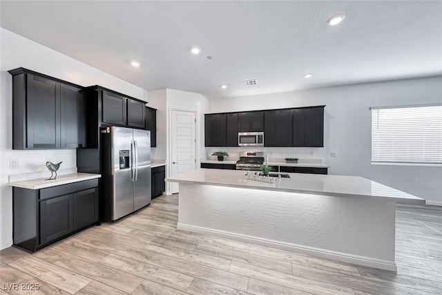 kitchen featuring a center island with sink, stainless steel appliances, light countertops, visible vents, and dark cabinetry